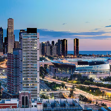 Twilight view of Chicago’s lakefront with McCormick Place and surrounding high-rises, illuminated streets in the foreground, and Lake Michigan stretching into the distance.